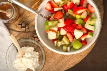 Fruit salad in white bowl on wooden board.