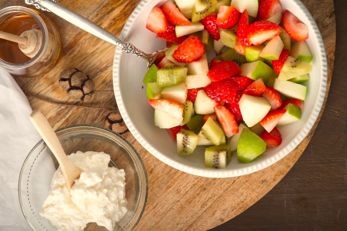Fruit salad in white bowl on wooden board.