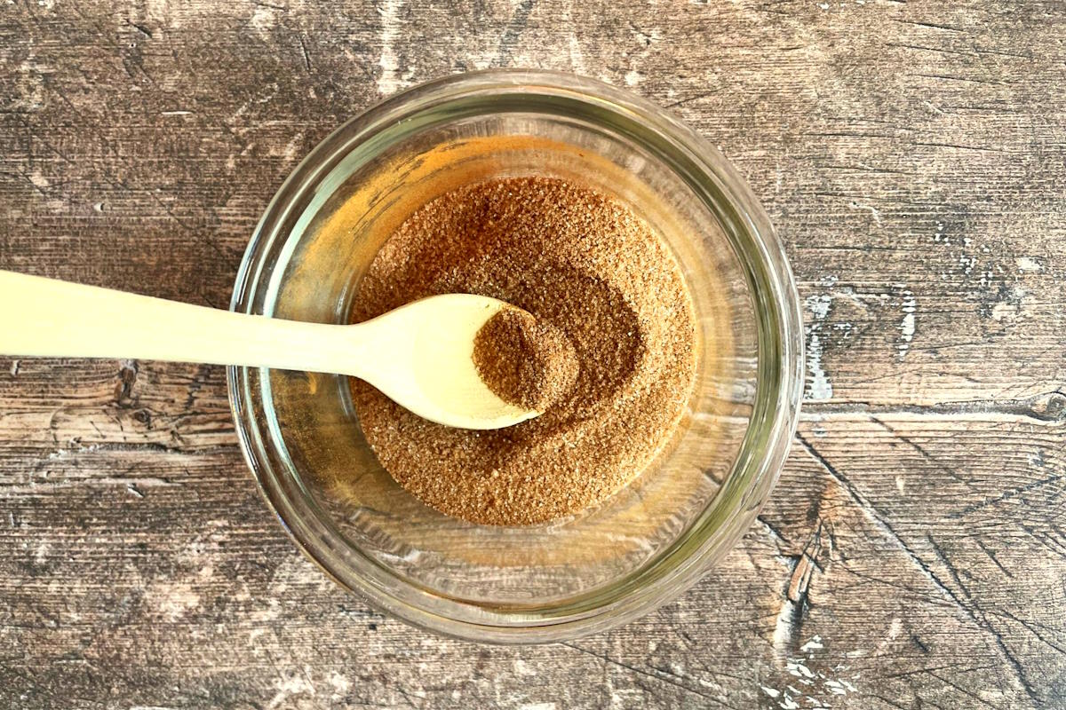 Cinnamon sugar in bowl with small wooden spoon.