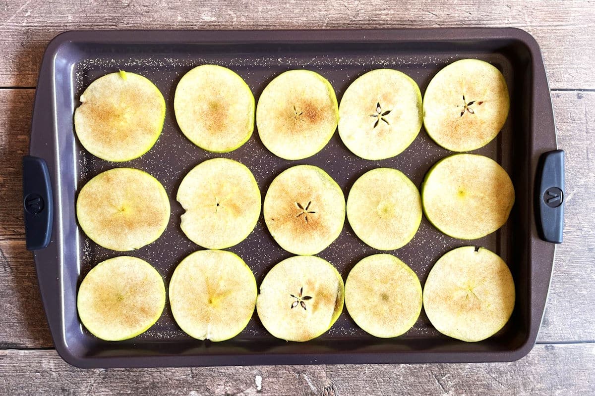 Sliced apples with cinnamon sugar on baking sheet.