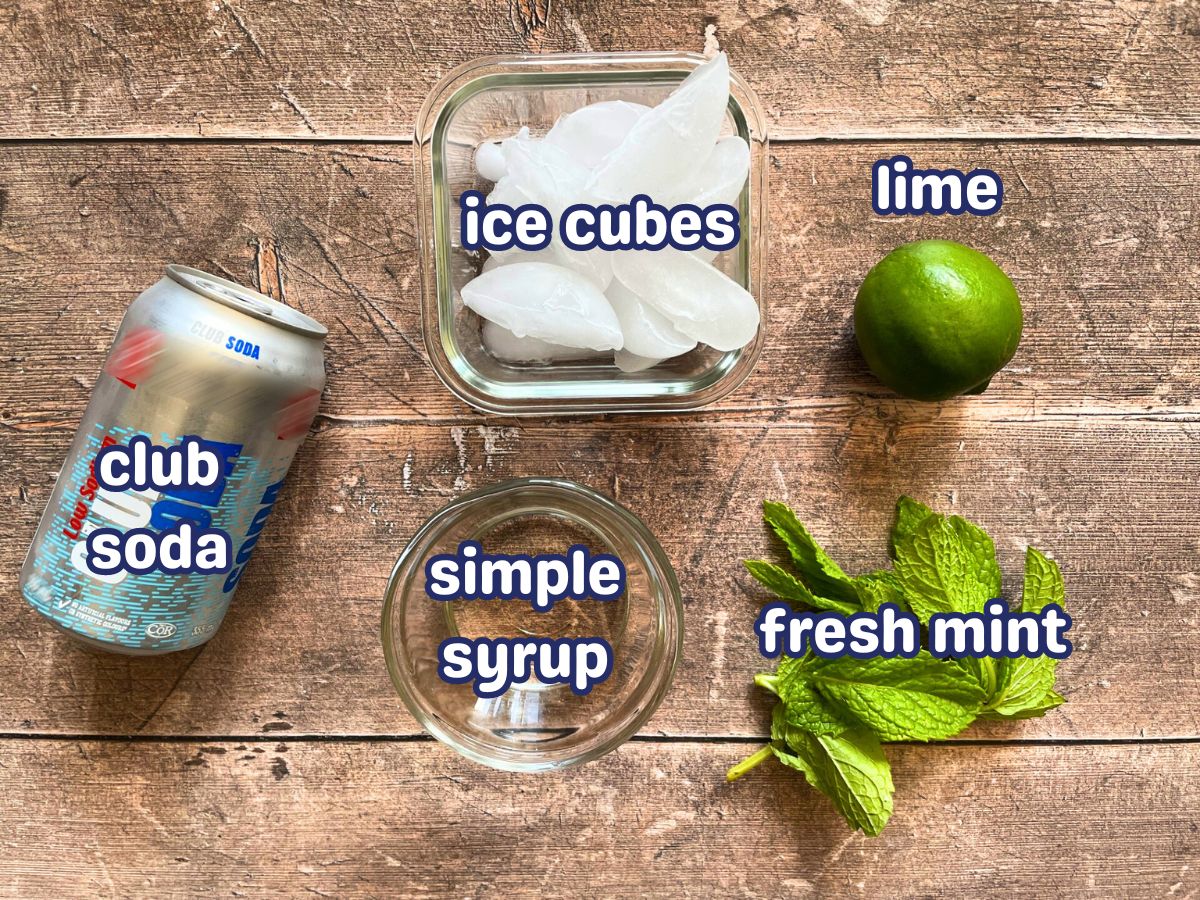 Classic mojito mocktail ingredients prepped and labeled on wooden background.