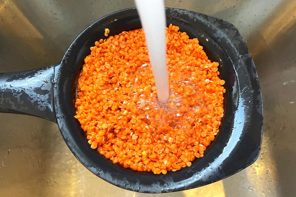 Red lentils getting rinsed with cold water in sieve.