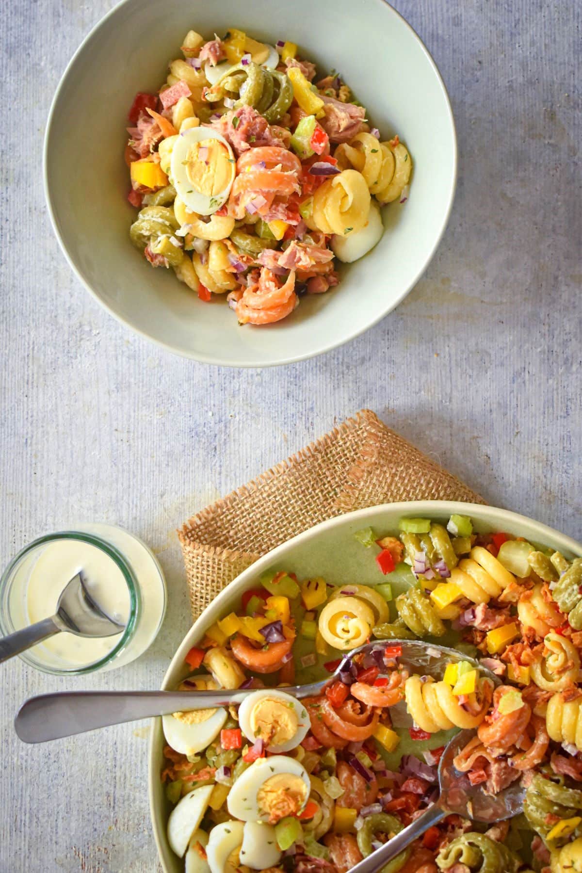 Creamy tuna pasta salad in bowls with spoons and dressing on the side.