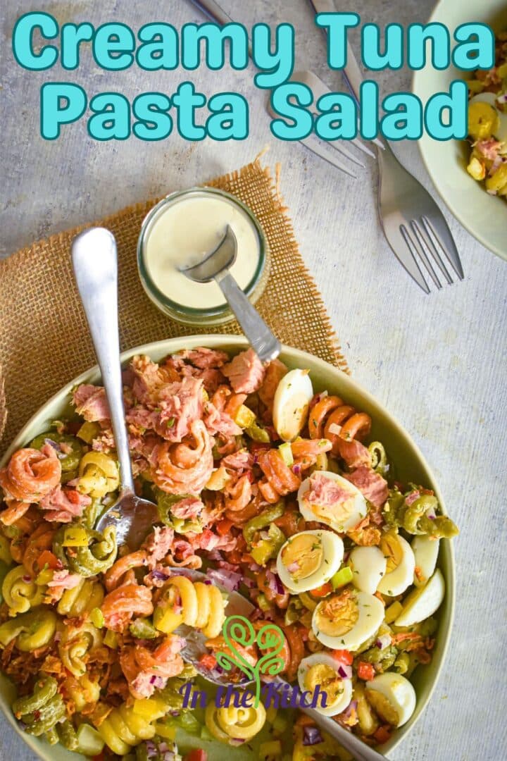 Tuna pasta salad in bowl with spoons and creamy sauce on the side.