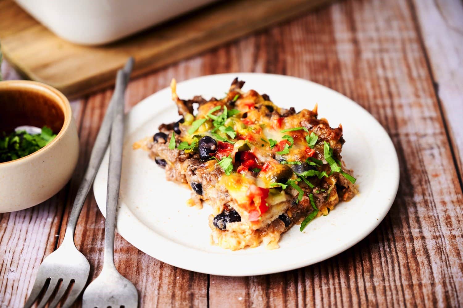Piece of creamy burrito casserole on white plate with forks.