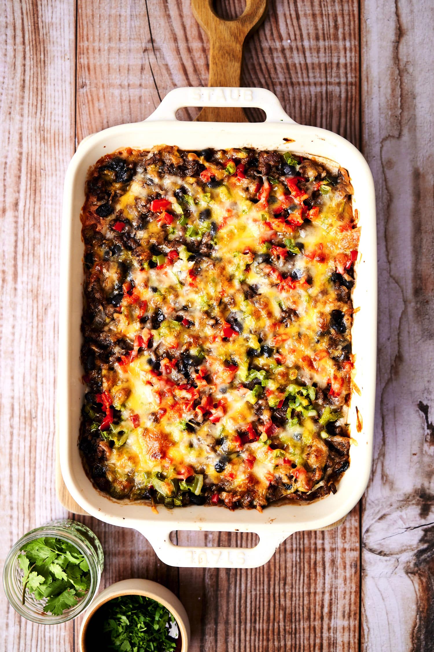 Creamy burrito casserole in casserole dish on wooden background.