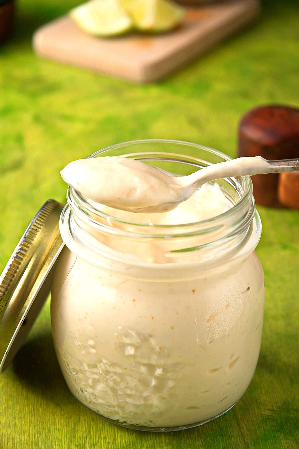 Creamy lime sauce in jar with spoon on lime green background.