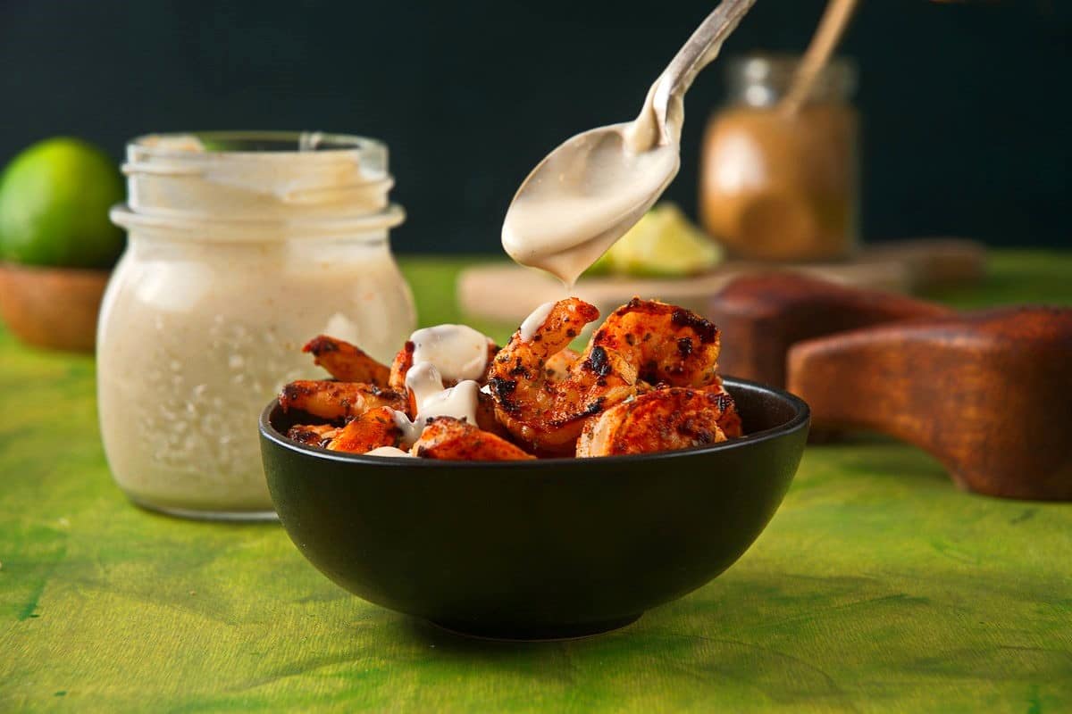 Creamy lime sauce spooned over bowl of spicy shrimp.