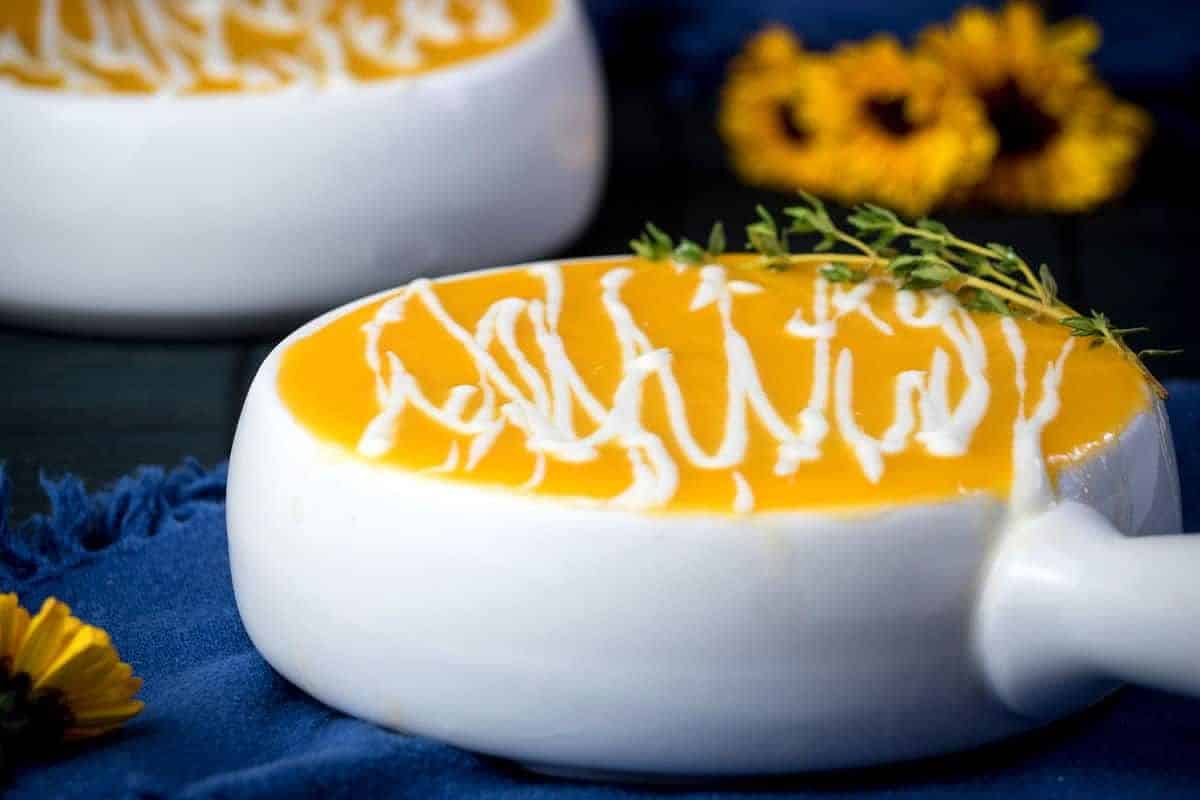 Pumpkin soup in soup bowl with Greek yogurt drizzle and thyme.