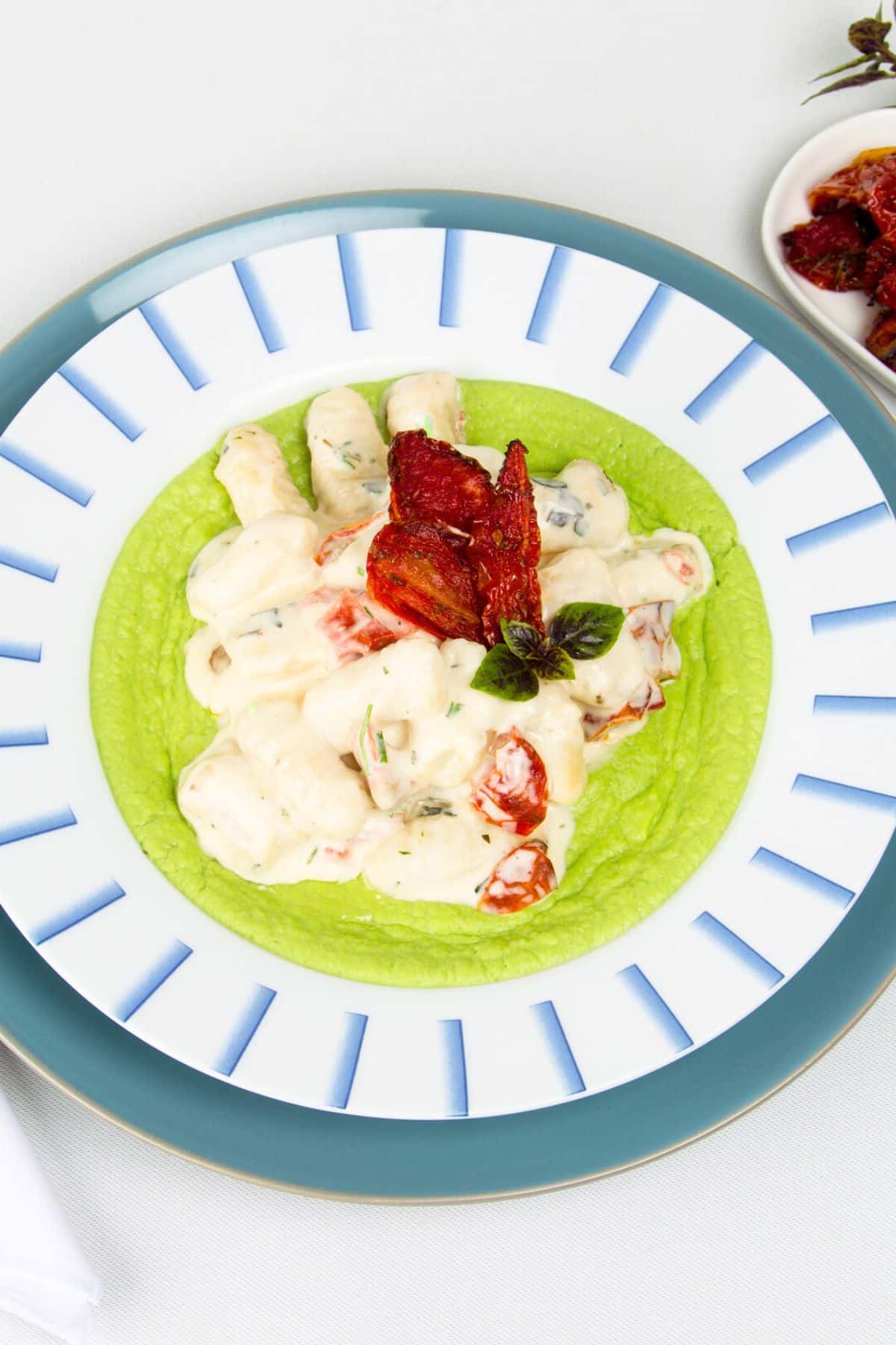 Creamy tomato gnocchi on blue and white plate with sundried tomatoes and pea purée.