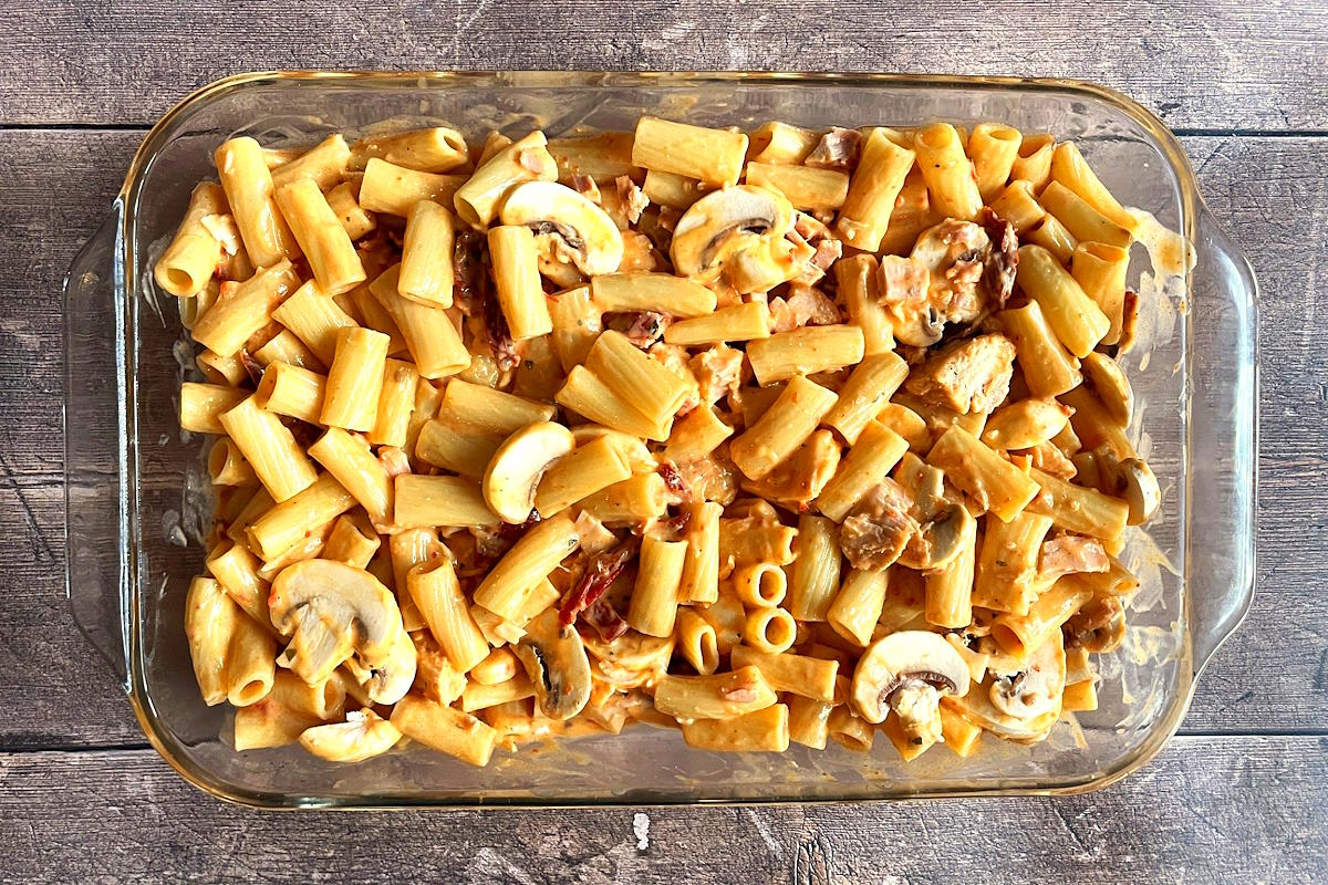 Short cut pasta noodles with sauce, mushrooms and sun-dried tomatoes in casserole dish.