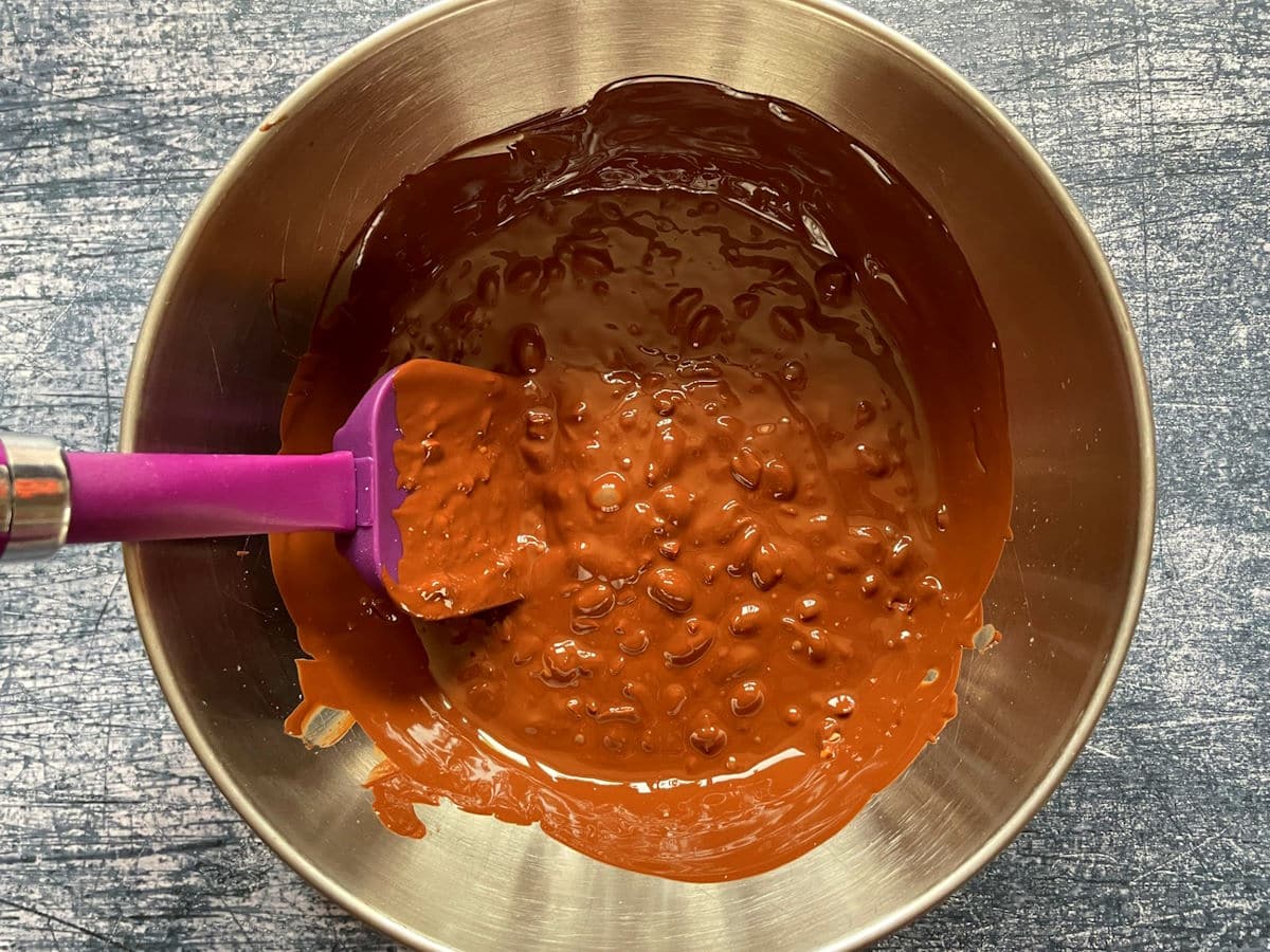 Melted chocolate combined with peanuts in metal bowl.