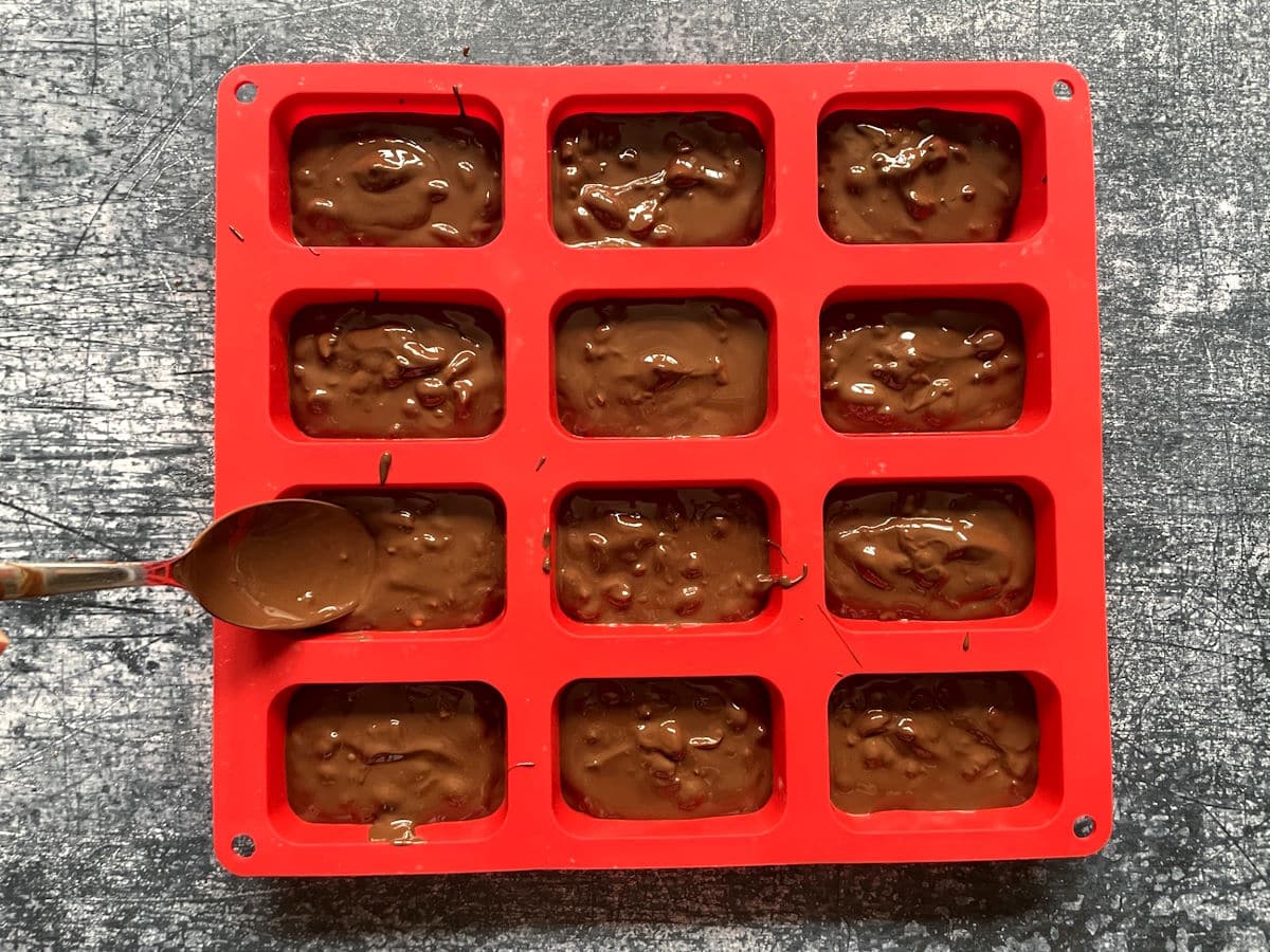 Chocolate and peanuts mixture in candy mold with spoon.