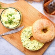 Dill pickle cream cheese bagel spread on bagel and in small glass dish on cutting board.