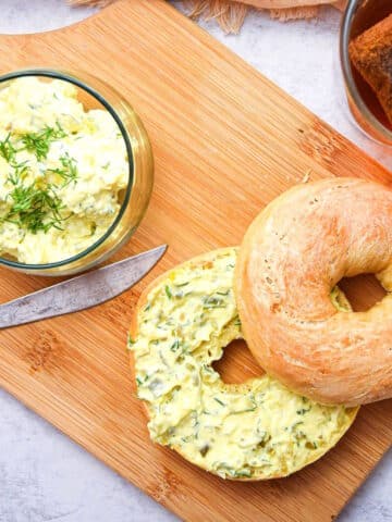 Dill pickle cream cheese bagel spread on bagel and in small glass dish on cutting board.