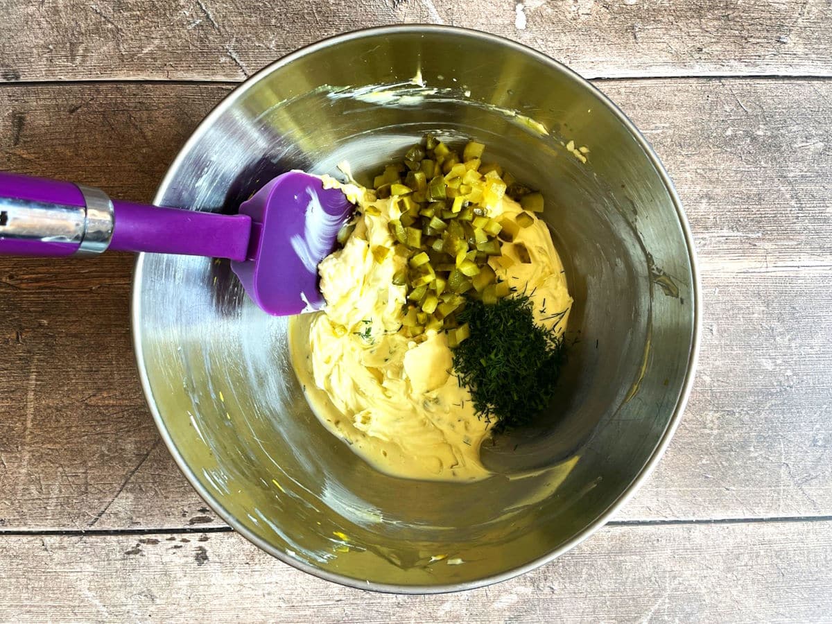 Dill pickle cream cheese spread ingredients in bowl with spatula.