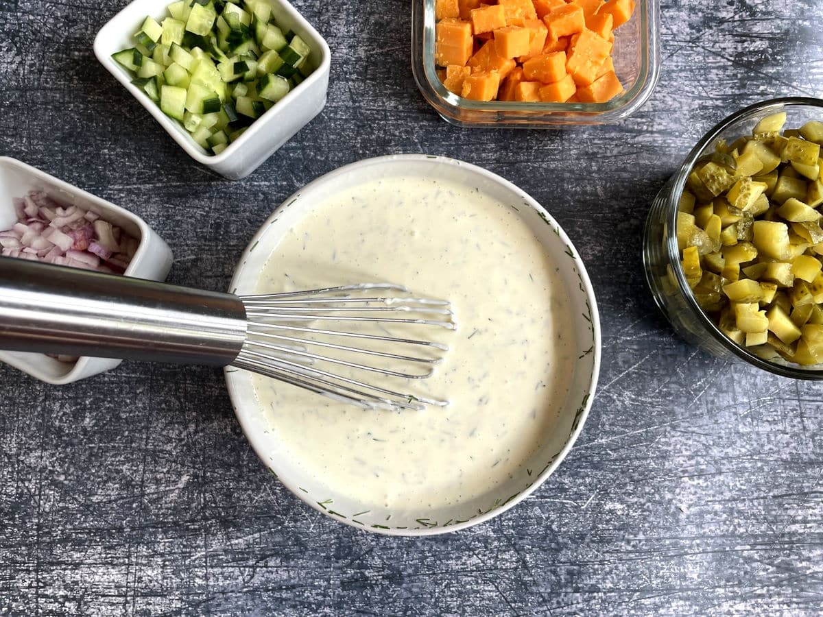 Dill pickle pasta salad dressing in bowl with whisk.