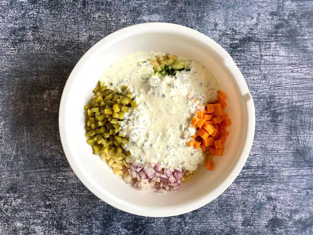 Dill pickle pasta salad ingredients with dressing in white bowl.
