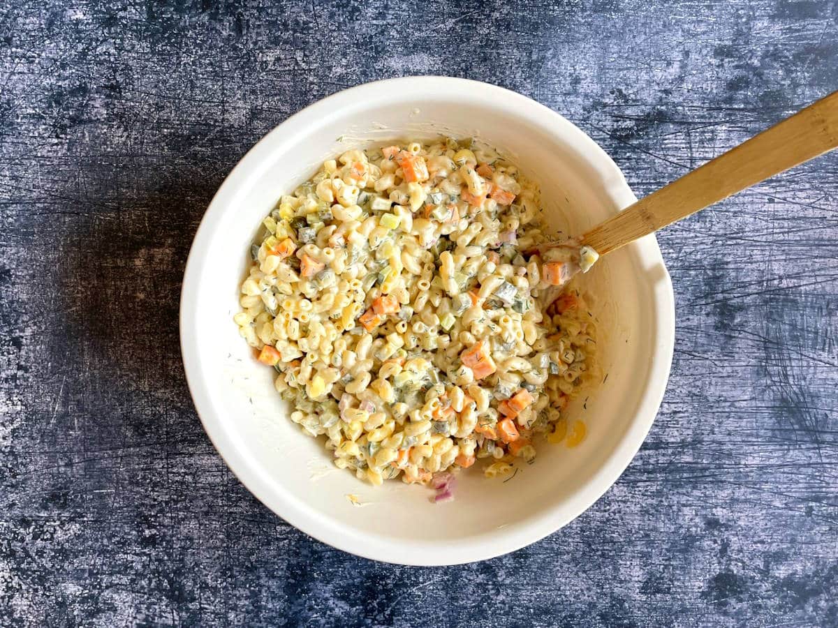 Dill pickle pasta salad combined in white bowl with wooden spoon.