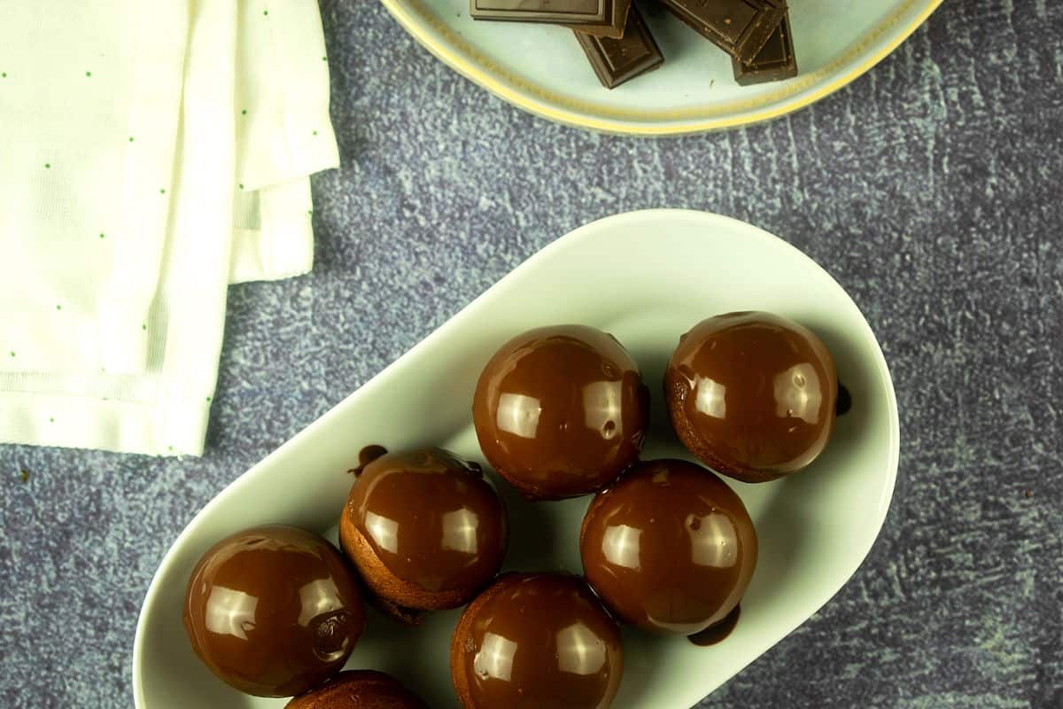 Chocolate covered donut holes on serving tray with pieces of chocolate bar on the side.