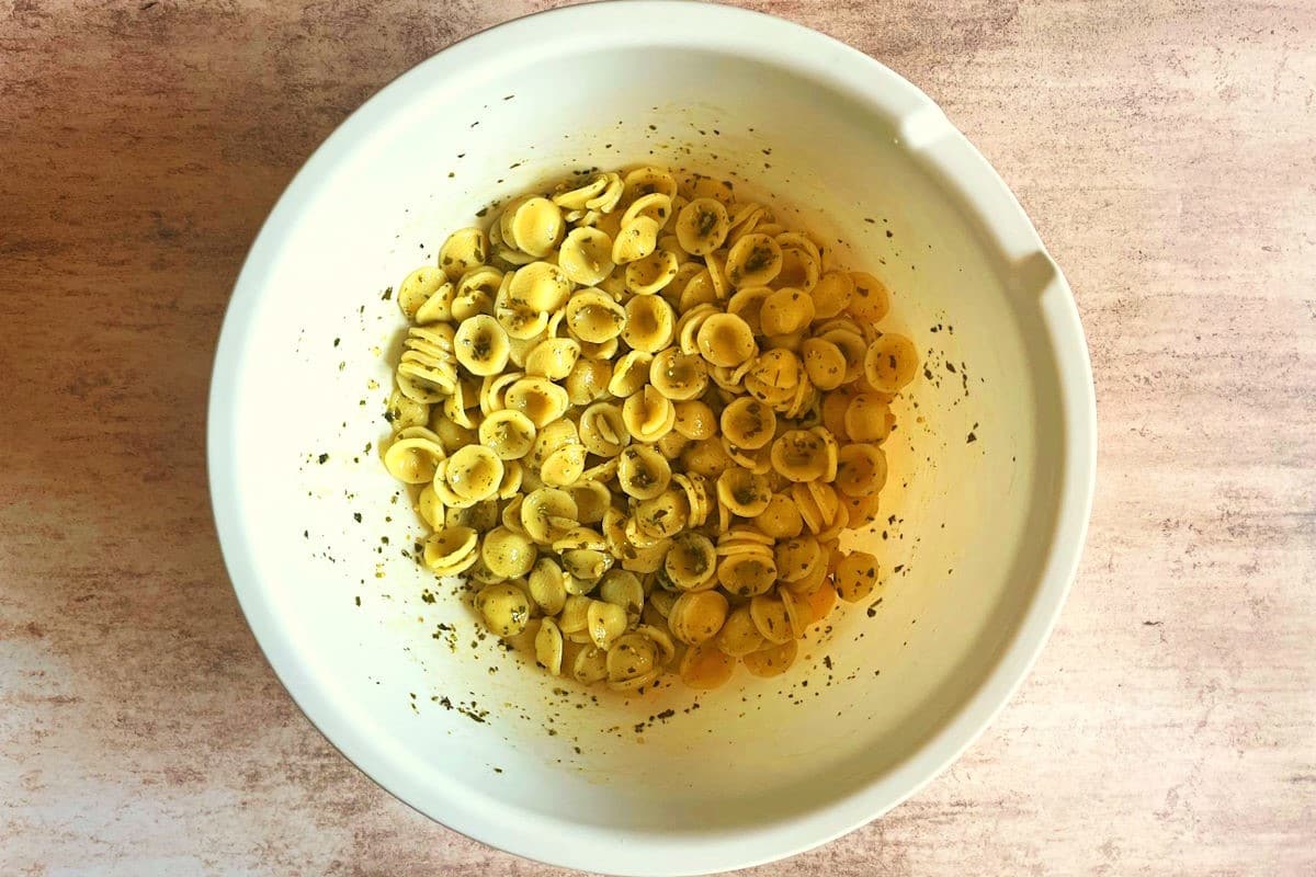 Orecchiette pasta combined with basil pesto in large bowl.