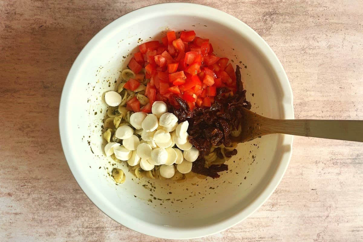 Caprese pasta salad ingredients in large bowl with wooden spoon.