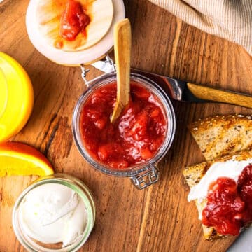 Strawberry orange compote in jar with spoon and toast on the side.