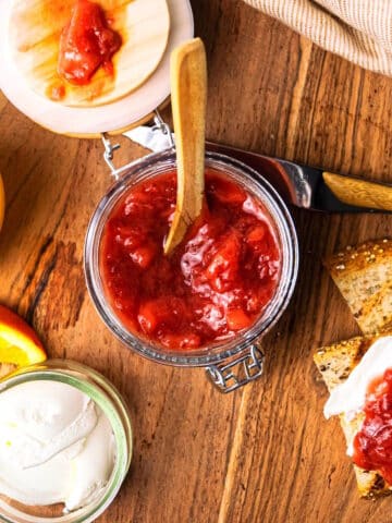 Strawberry orange compote in jar with spoon and toast on the side.