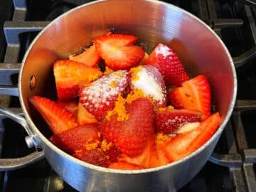 Strawberries, sugar and orange in saucepan.