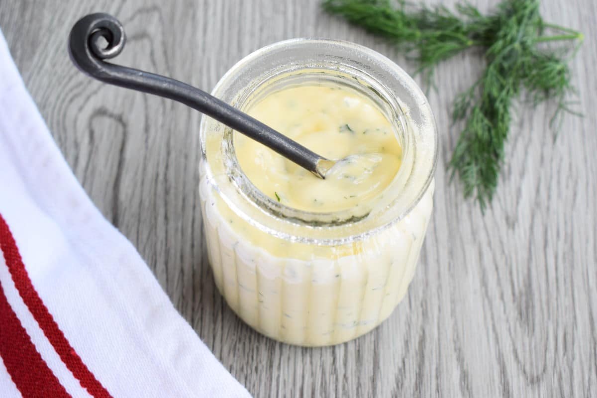 Honey dill sauce in small jar with mini serving spoon, fresh dill on the side.