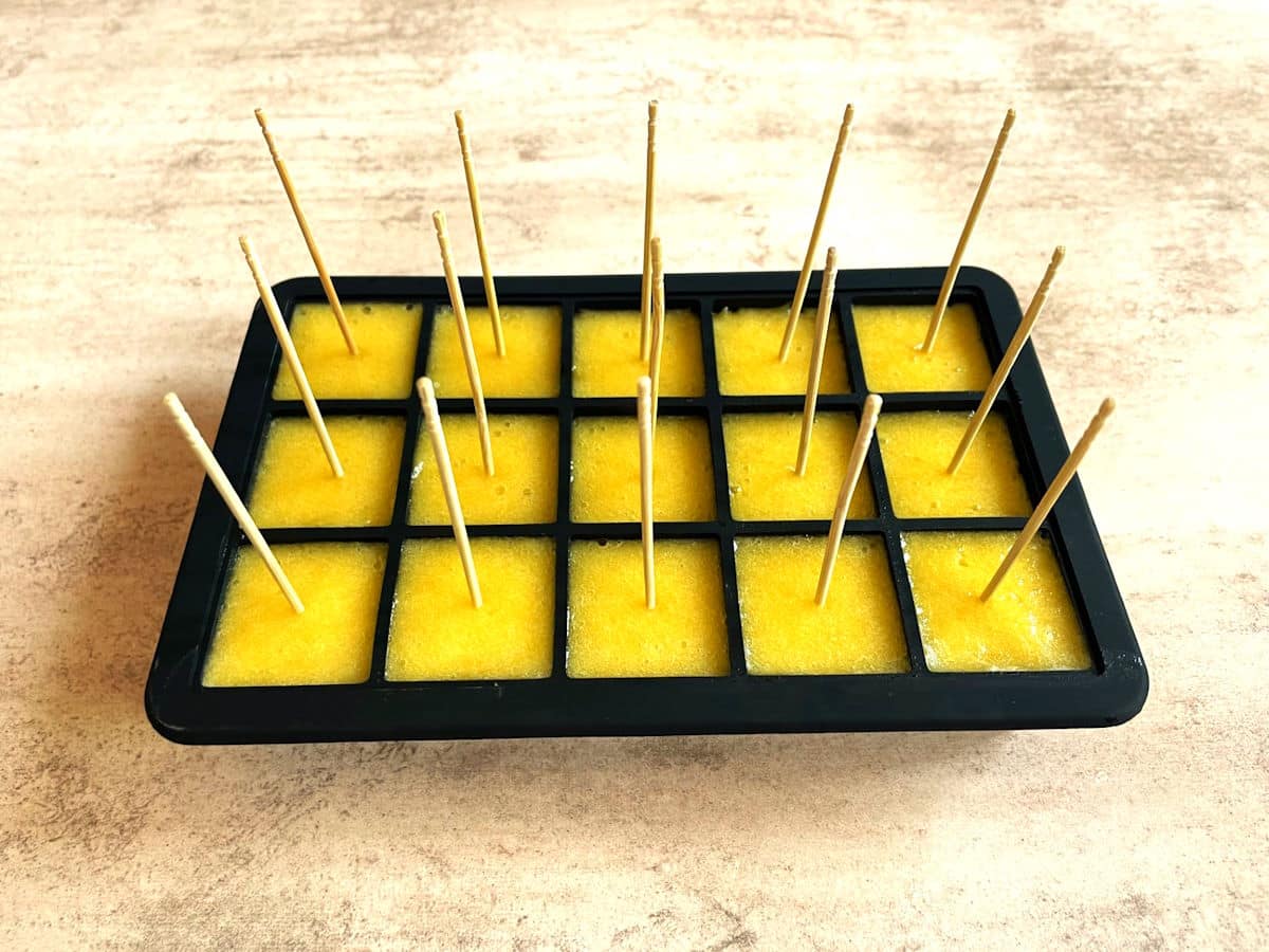 Frozen peach purée cubes in ice cube tray with cocktail picks.