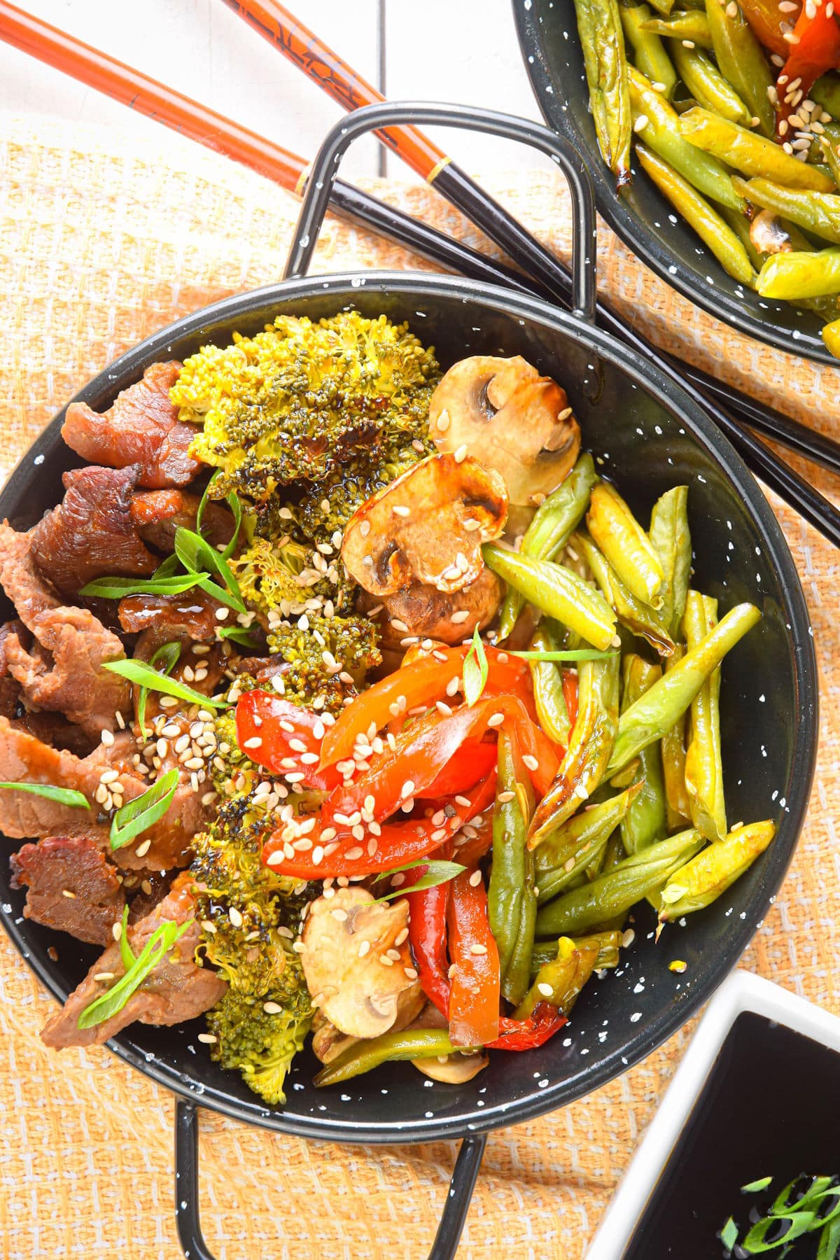 Beef and broccoli in a black bowl, topped with sesame seeds.