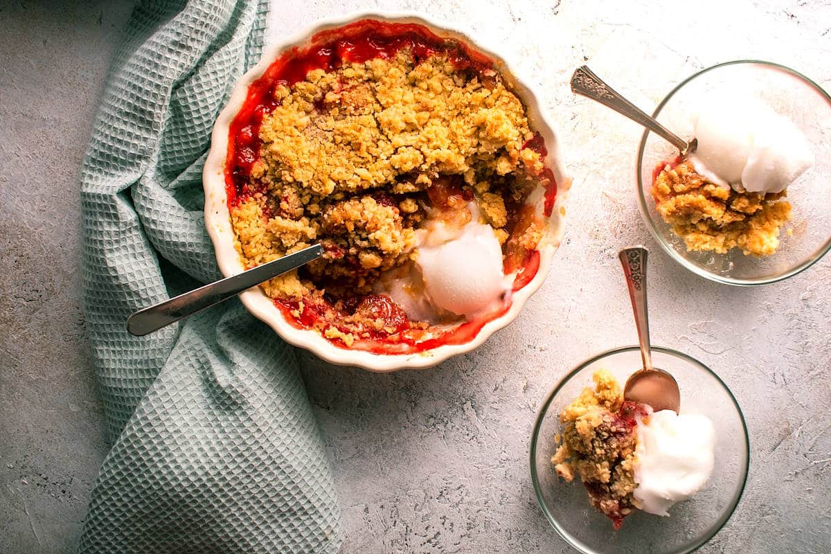 Strawberry crumble with ice cream in dessert bowls with spoons.