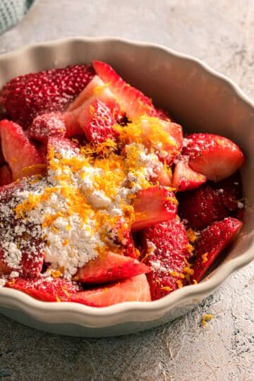 Strawberries, cornstarch and orange zest in tart dish.