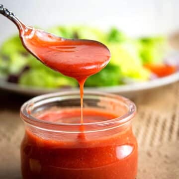 Strawberry vinaigrette dressing drizzling down spoon into small jar.