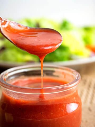 Strawberry vinaigrette dressing drizzling down spoon into small jar.
