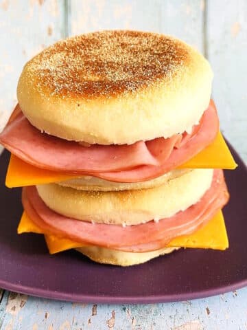 English muffin sandwiches stacked on purple plate.