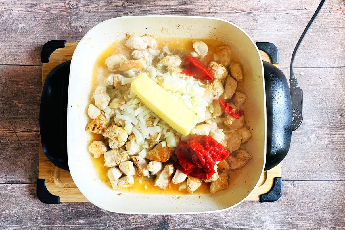 Butter chicken ingredients cooking in electric skillet.