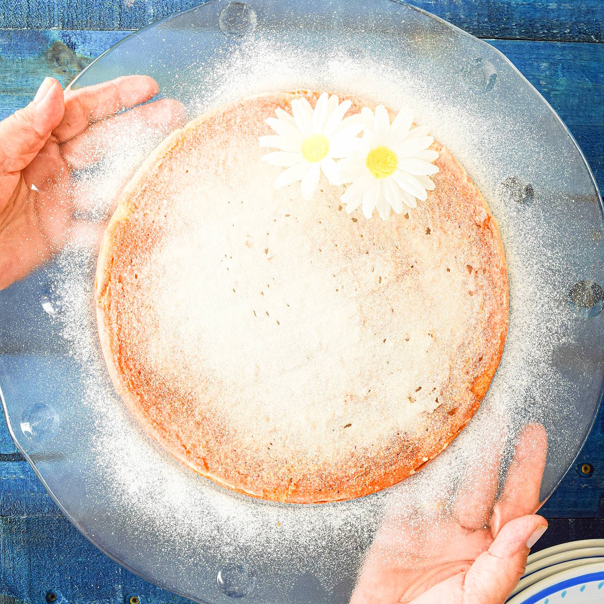 Yogurt cake on clear plate held by hands.