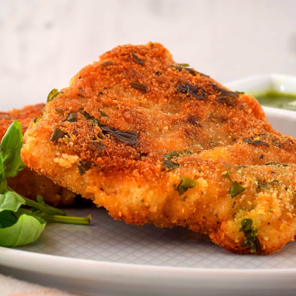 Electric skillet fried fish on white plate with fresh basil.