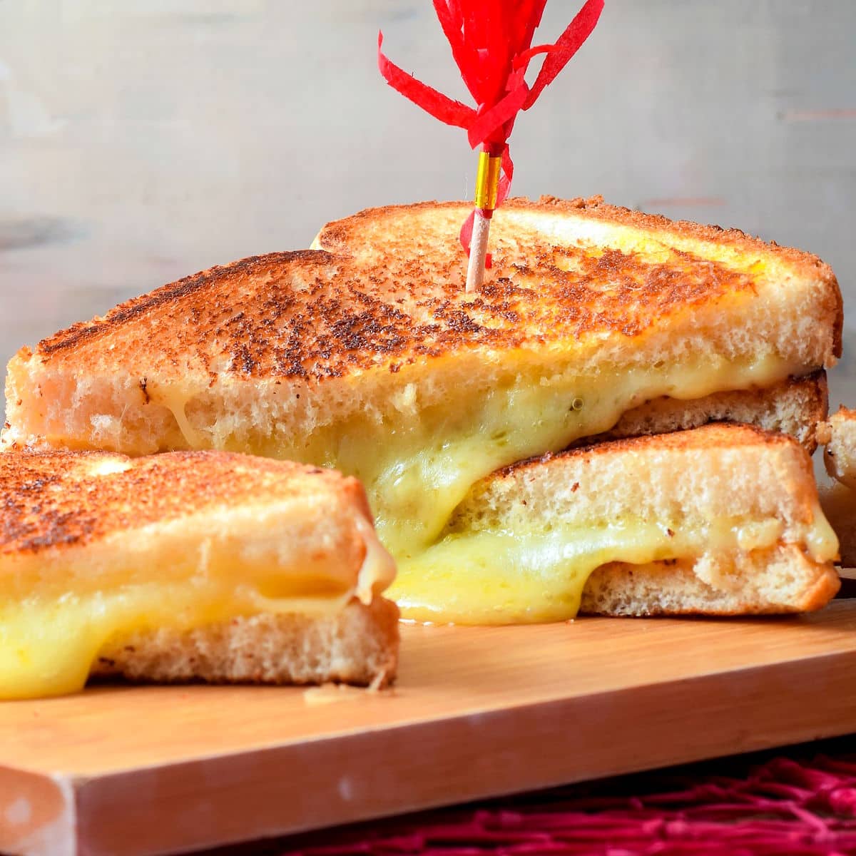 Electric skillet grilled cheese sandwiches stacked on serving board.