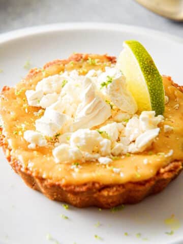 Key lime pie on plate topped with lime and broken meringue cookies.