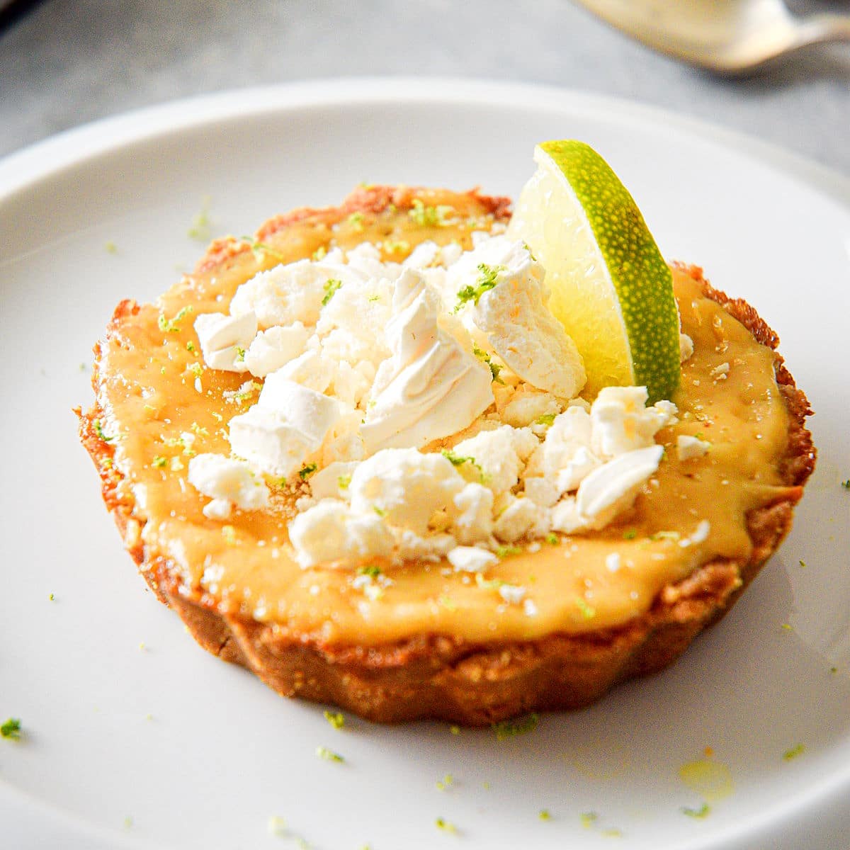 Key lime pie on plate topped with lime and broken meringue cookies.
