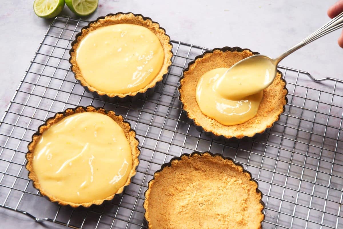 Raw key lime pies getting filled on baking rack.