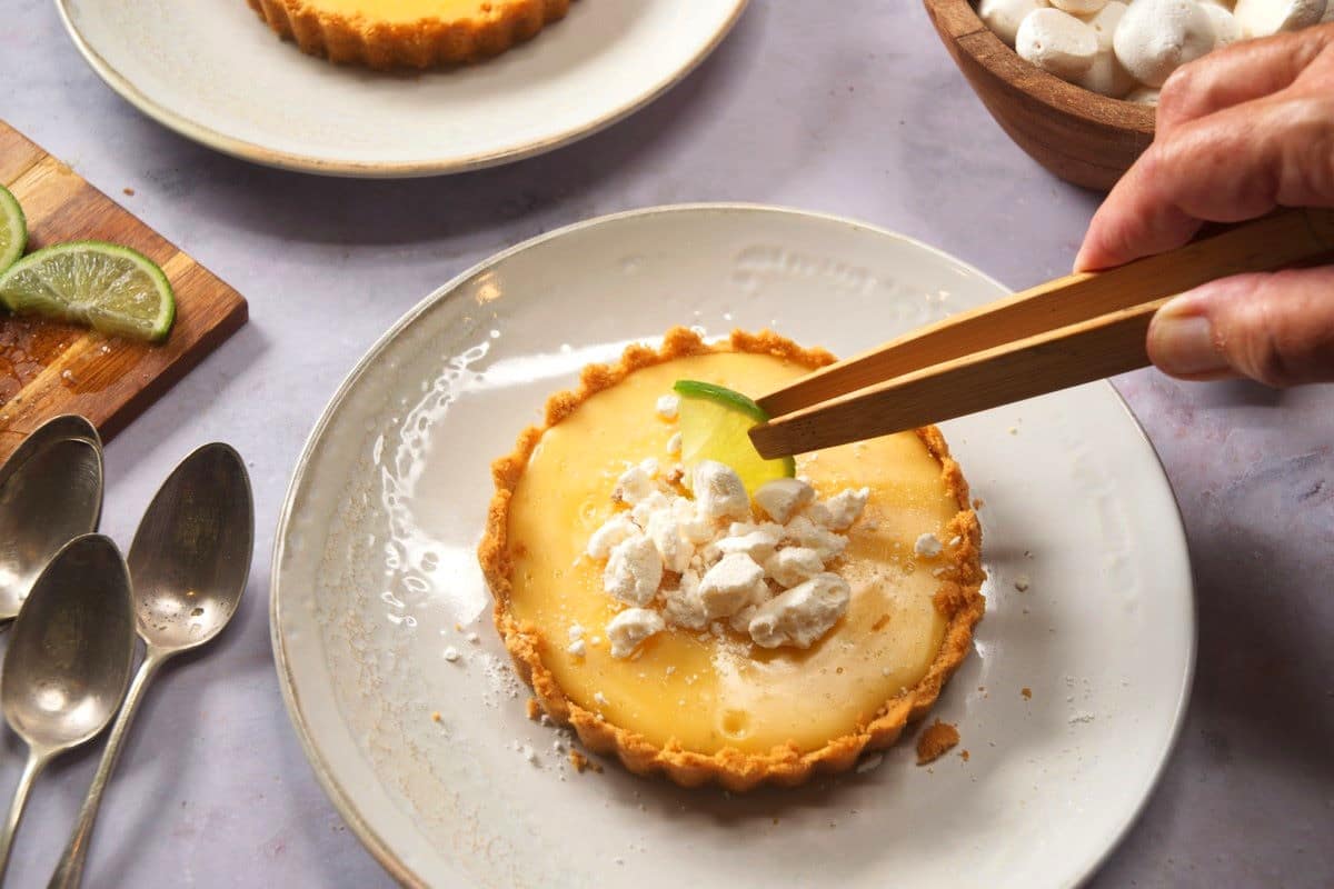 Key lime pie getting topped with broken meringue and lime slices.