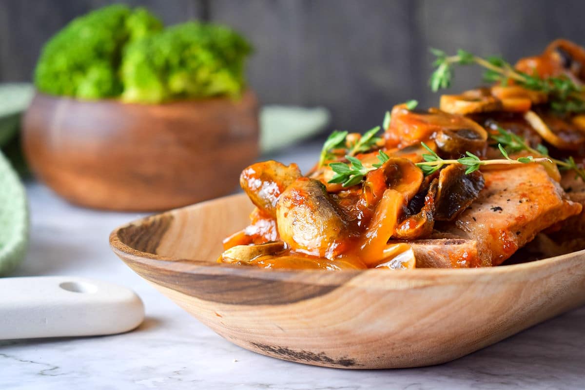 Pork chops with gravy, mushrooms and fresh thyme in serving dish.