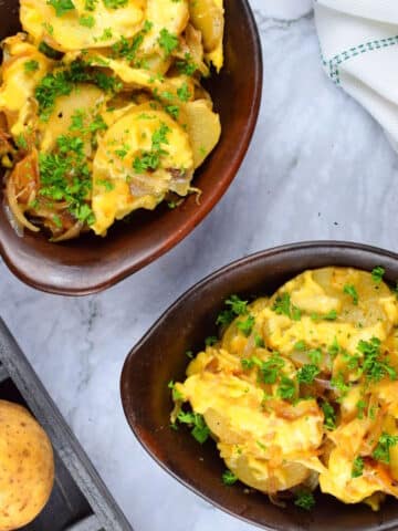 Cheesy scalloped potatoes in brown bowls on marble background.