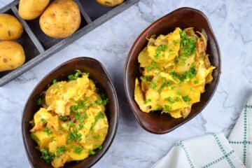 Cheesy scalloped potatoes in brown bowls with whole Yukon Gold potatoes on the side.