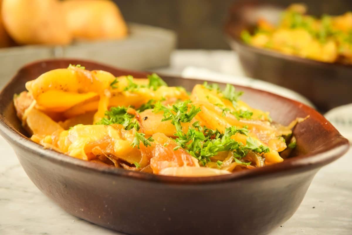 Cheesy scalloped potatoes in brown bowl topped with parsley.