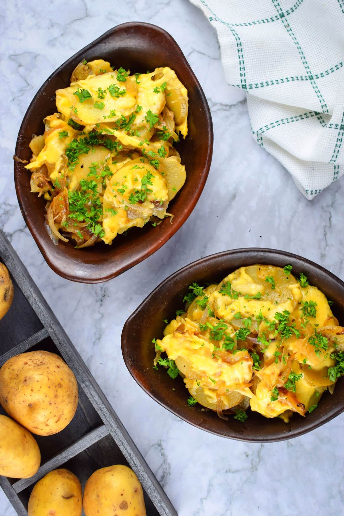 Cheesy scalloped potatoes in brown bowls, yellow potatoes on the side.